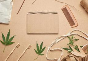 open notebook with empty sheets, a textile bag and disposable tableware from brown craft paper, green hemp leaves photo