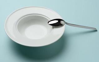 empty white ceramic plate and metal spoon on blue background photo
