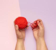 two female hands hold a ball of red woolen threads photo