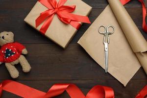 roll of brown kraft packaging paper, box tied with a red silk ribbon, scissors photo