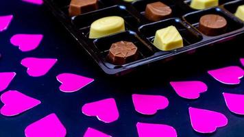 delicious chocolate surrounded by pink hearts on black background photo