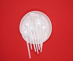 round plate and stack of plastic forks and spoons on red background photo