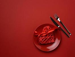 round ceramic plate and fork with knife on red background, festive table setting photo