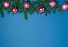 green spruce branches, pink shiny Christmas balls on a blue background photo