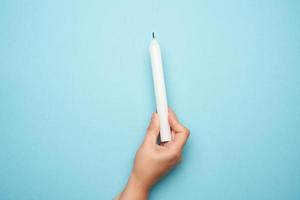 female hand holding a white wax candle on a blue background photo