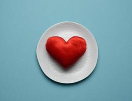 red heart lies in a white ceramic plate on a blue background photo