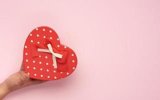 female hands hold a paper closed red box in the shape of a heart on a pink background photo