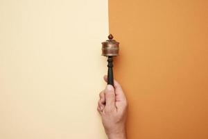 copper prayer drum on a stick in a male hand on a brown background photo