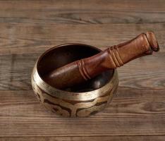 Tibetan singing copper bowl with a wooden clapper on a brown wooden table photo