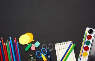 colorful wooden pencils, scissors, notepads and paint for drawing on a blank black chalk board photo