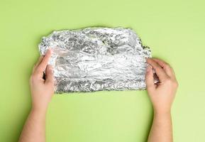 two female hands holds crumpled silver foil on a green background photo