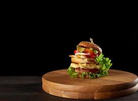 big delicious burger with meat cutlet, cheese, fried egg, tomatoes, cucumber slices and green lettuce photo