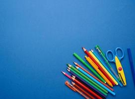 tijeras de plástico y lápices de madera multicolores sobre un fondo azul foto