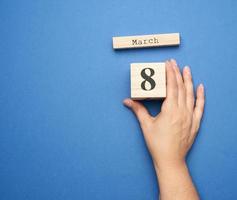 mano femenina sostiene calendario de madera con fecha del 8 de marzo foto