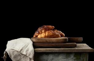 baked croissants on brown kitchen board, black background photo