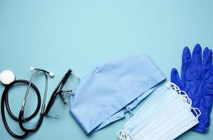 textile blue cap, disposable medical mask, pair of gloves and plastic glasses on a blue background photo