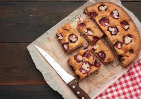 sliced baked pie with plums on a wooden plank background photo