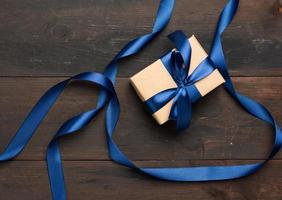 caja rectangular envuelta en papel marrón y atada con una cinta de seda azul con un lazo