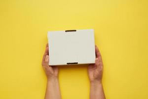 two female hands hold closed paper box on a yellow background photo