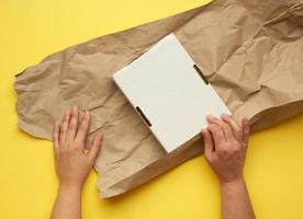 rectangular white cardboard box and two female hands are wrapped with brown paper photo