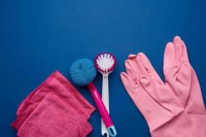 guantes de goma rosa para limpiar, esponjas rosas, cepillos sobre un fondo azul foto