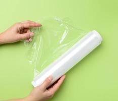 two female hands hold a roll of transparent cling film for packaging products photo