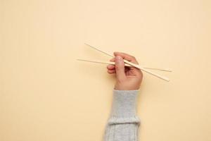 a pair of wooden chopsticks in a female hand on a beige background photo