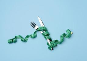 fork and knife wrapped in green measuring tape on blue background photo