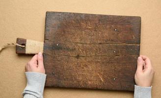 dos manos femeninas sostienen una vieja tabla de cortar de madera rectangular marrón vacía foto