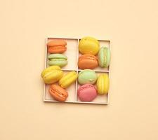 wooden box and baked multi-colored macarons cookies on a beige background photo