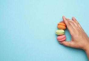 female hand holds three round baked macarons cookies on a blue background photo