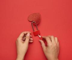 two female hands hold a metal lock and keys on a red background photo