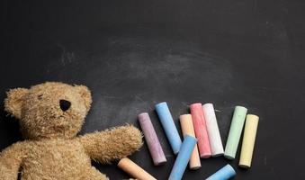 oso de peluche marrón y lápices de colores en pizarra negra foto