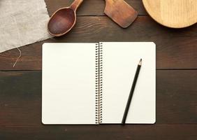 open notebook with blank white sheets and kitchen utensils on brown wooden table photo