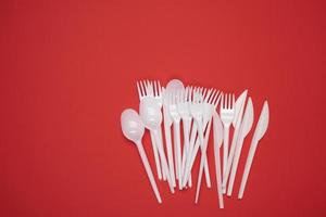 stack of plastic forks and spoons on red background, top view photo