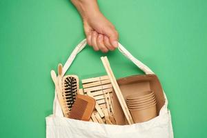 mano femenina sostiene una bolsa textil llena de artículos domésticos reciclables, fondo verde foto