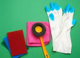 white rubber gloves for cleaning, multi-colored sponges, brushes on a green background photo