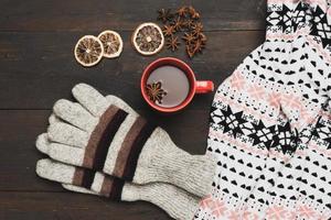 gray knitted mittens and red cup with a drink on a brown wooden table photo