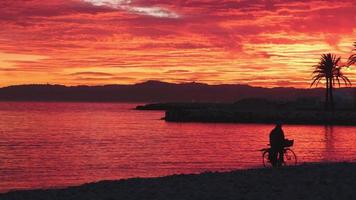 silhuett av de man med en cykel gående på de strand på en dramatisk solnedgång, panorama- marinmålning antal fot 4k. video