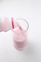 Strawberry-flavored pink milk is being poured from a bottle into a glass on a white background. photo
