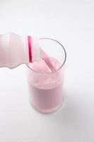 Strawberry-flavored pink milk is being poured from a bottle into a glass on a white background. photo