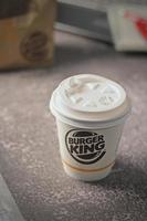 Washington, EE.UU. - 18 de enero de 2023 taza de café Burger King con portátil y portátil en una mesa gris con iluminación de estudio, Burger King es una comida popular en Estados Unidos. foto