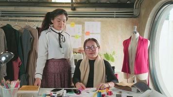 equipo de moda, diseñadora asiática y asistente adolescente en el estudio, brazos cruzados y sonrisa, feliz trabajando con hilos coloridos y costura para el diseño de vestidos, boutique profesional sastre pyme emprendedora. video