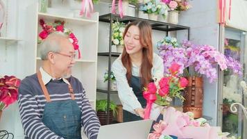 asiatisk äldre manlig blomsterhandlare ägare diskuterar med ung skön kvinna anställd handla om blommig bukett arrangemang och dekoration för företag, Lycklig arbete i färgrik blomma affär Lagra, e-handel sme. video