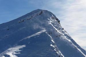 View of mountain peak on a very windy sunny day. Wind swirling the snow in the air. Outdoor winter hike. Winter traveling. Adventure and exploring the mountains. photo