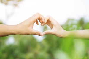 Young couple lover show holding hands make heart shape over in public parks. photo