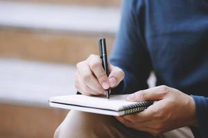 close up hand young man are sitting using pen writing Record Lecture note pad into the book on the table wood. photo