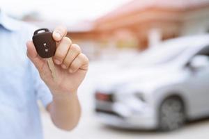 Business man hand holding car keys front with new car on background. parking in front of the house. transportation concept. Leave copy space to write messages text. photo