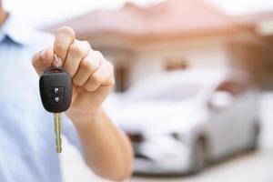 Business man hand holding car keys front with new car on background. parking in front of the house. transportation concept. Leave copy space to write messages text. photo
