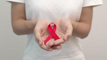 mano Tenere rosso nastro per dicembre mondo AIDS giorno, acquisito immune carenza sindrome, multiplo mieloma cancro consapevolezza mese e nazionale rosso nastro settimana. assistenza sanitaria e mondo cancro giorno video